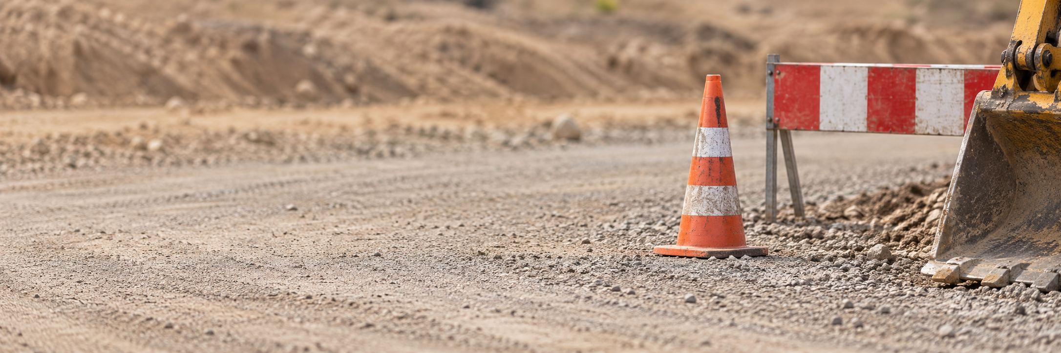Illustrative roadworks scene with a cone, barrier and excavator bucket